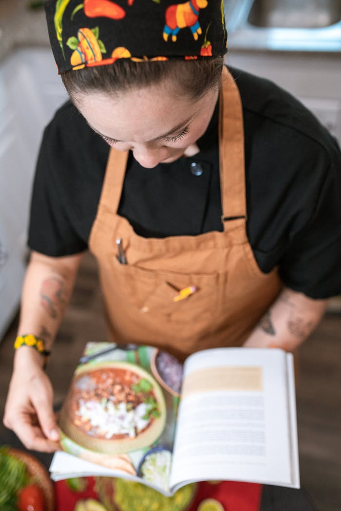 An adult female chef in a kitchen reading a cookbook. Overhead view, indoors.
