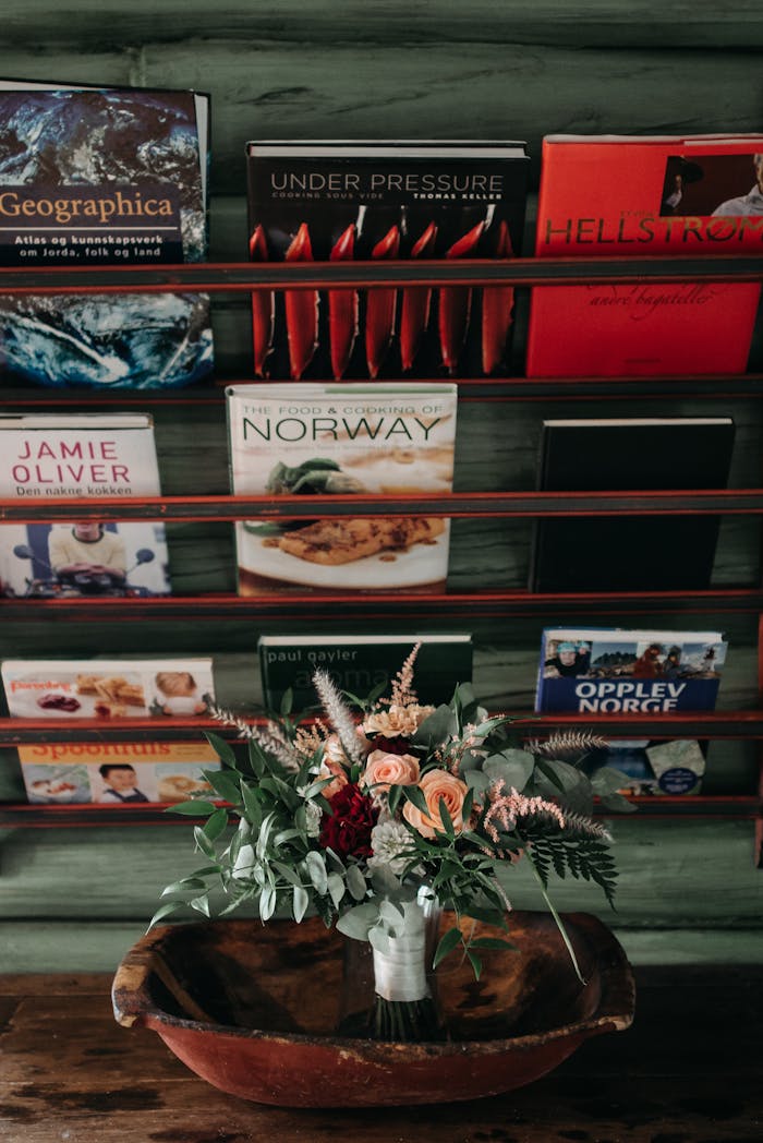 Vertical shot of a bookshelf with assorted books and a floral bouquet in a vase.