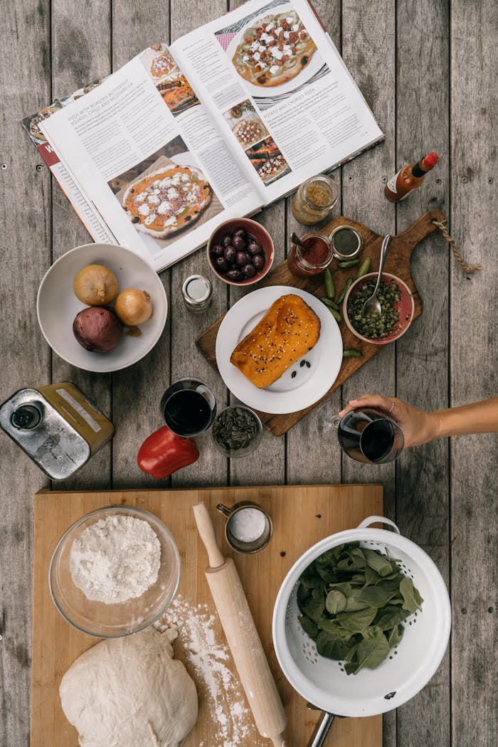 Top-down view of pizza ingredients and cookbook on a rustic wooden table.